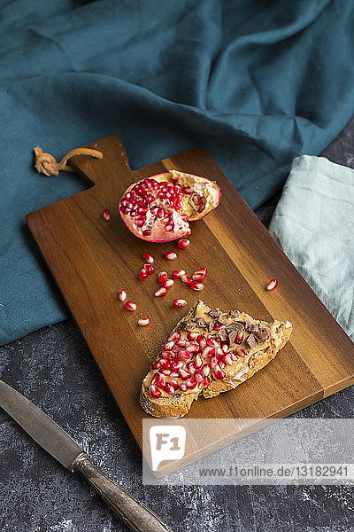 Brotscheibe mit Erdnussbutter  Granatapfelkernen und Schokoladenstücken auf Holzbrett