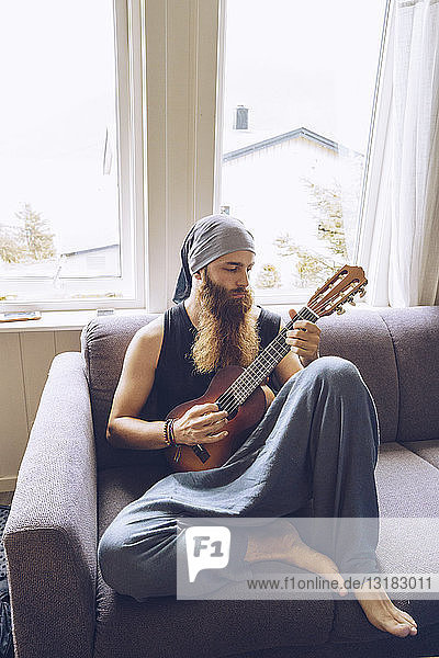 Bearded man playing guitar on couch