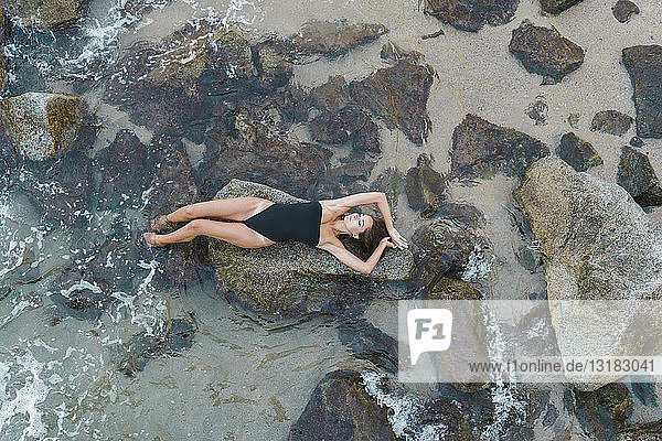 Draufsicht auf eine schöne junge Frau  die auf einem Felsen im Meer liegt