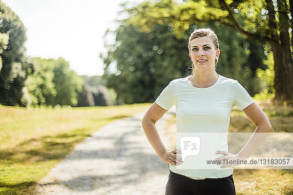 Porträt einer lächelnden  sportlichen jungen Frau  die in einem Park steht