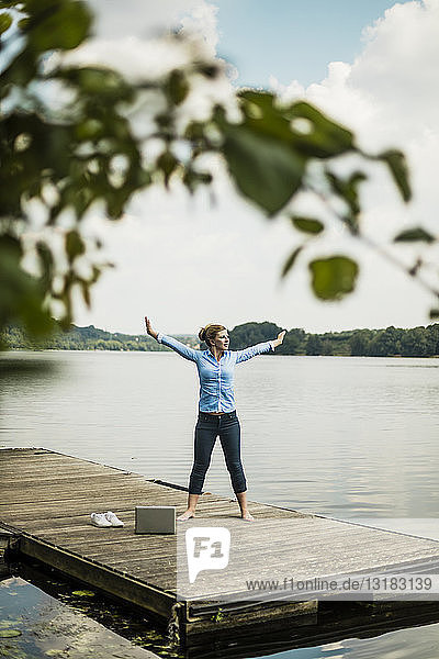 Frau  die sich auf einem Steg an einem See neben einem Laptop ausstreckt