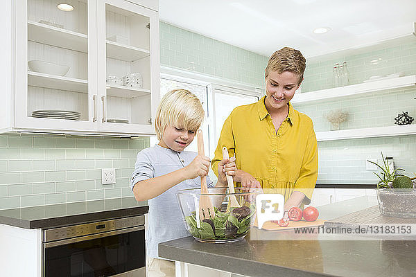 Lächelnde Mutter und Sohn bereiten gemeinsam Salat in der Küche zu