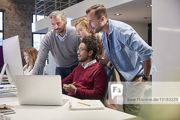 Colleagues looking over shoulder of young man working in modern office