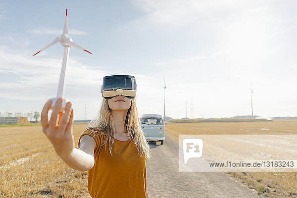 Young woman with VR glasses at camper van in rural landscape holding wind turbine model