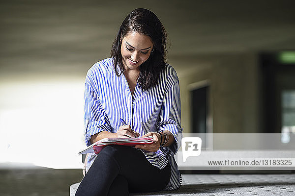Lächelnder Student sitzt auf einer Bank im Freien und macht Notizen in einem Notizbuch