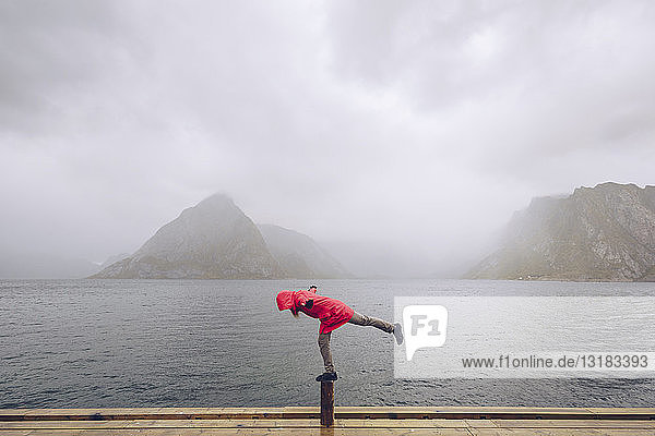 Norwegen  Lofoten  Hamnoy  Mann in roter Regenjacke auf Holzpfahl balancierend