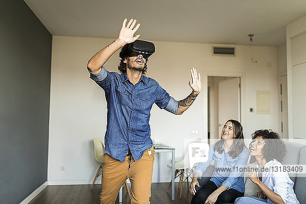 Two women watching man with VR glasses at home