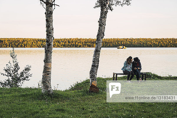 Junges Paar sitzt auf einer Bank am See und schaut sich die Bilder mit einer Kamera an