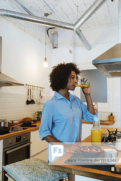 Frau frühstückt in ihrer Küche und trinkt Orangensaft