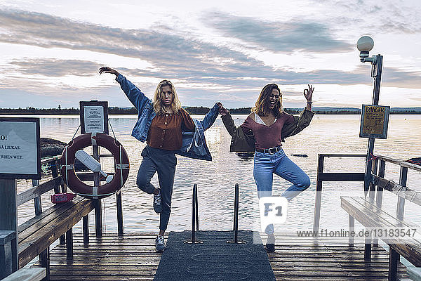 Two girl friends standing on one leg on a pier at Lake INari  Finland