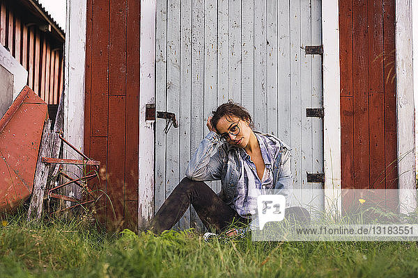 Porträt einer jungen Frau  die im Gras vor einer Holzhütte sitzt