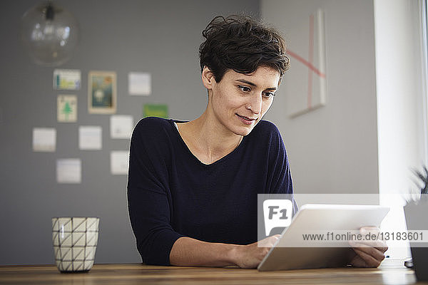 Woman sitting at table at home using tablet