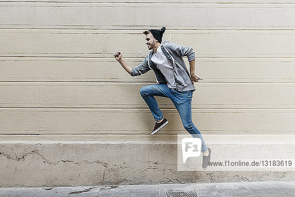 Happy young man jumping in front of a wall