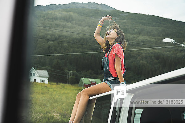 Junge Frau sitzt auf dem Dach eines Campingwagens