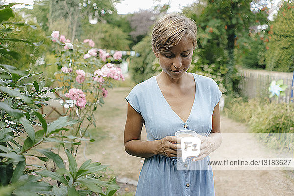 Frau steht im Garten mit einer Tasse Kaffee