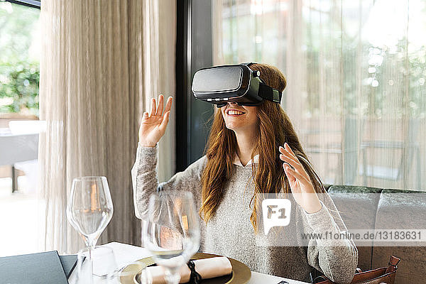 Frau  die in einem Restaurant am Tisch sitzt und eine VR-Brille trägt