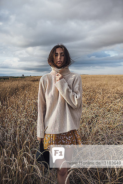 Porträt einer jungen Frau mit übergroßem Rollkragenpullover im Maisfeld stehend