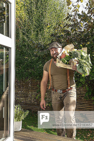 Reifer Mann  der in seinem Garten eine Kiste mit Gemüse trägt