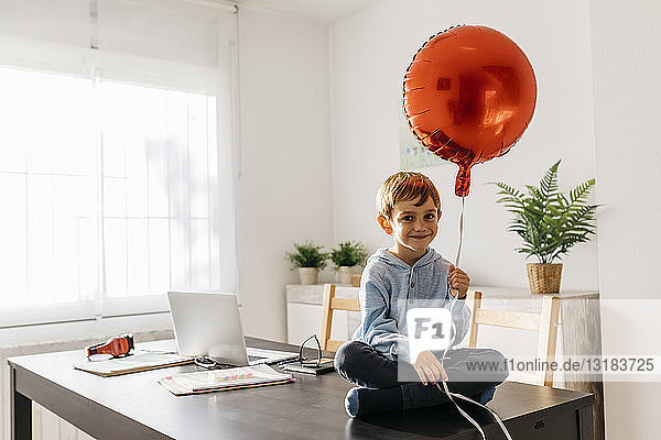 Junge sitzt auf dem Esstisch mit einem roten Ballon in der Hand