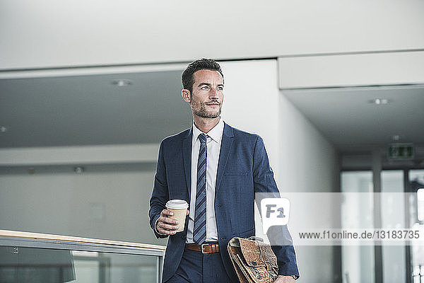 Geschäftsmann mit Aktenkoffer geht mit einer Tasse Kaffee in der Hand durch das Bürogebäude