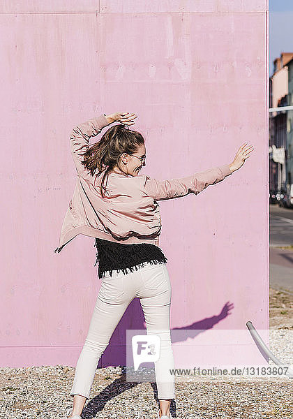 Glückliche junge Frau bewegt sich vor rosa Wand