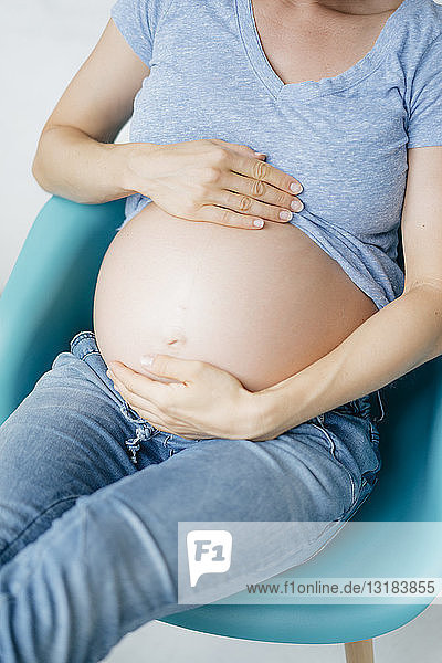 Nahaufnahme des Bauches einer schwangeren Frau  die auf einem Stuhl sitzt