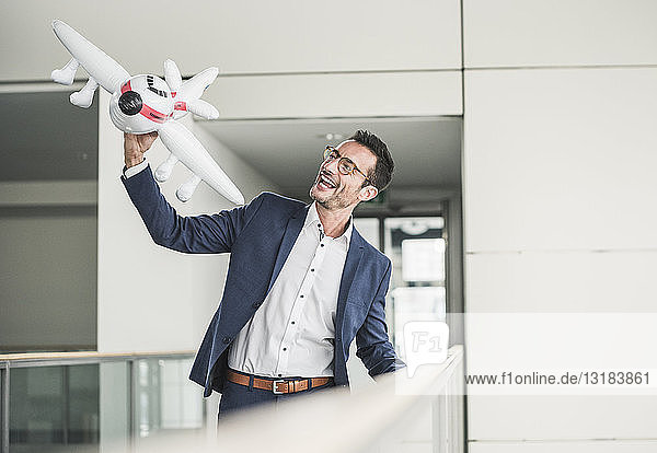 Laughing businessman playing with toy aeroplane in office building