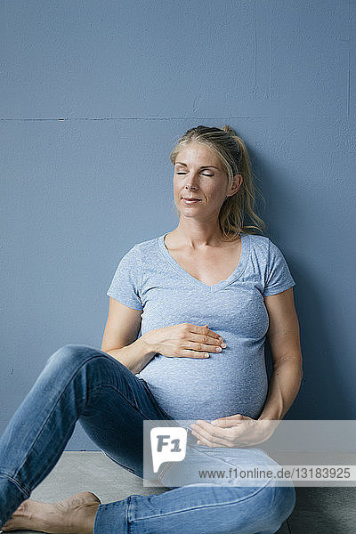 Porträt einer lächelnden schwangeren Frau  die mit geschlossenen Augen auf dem Boden sitzt