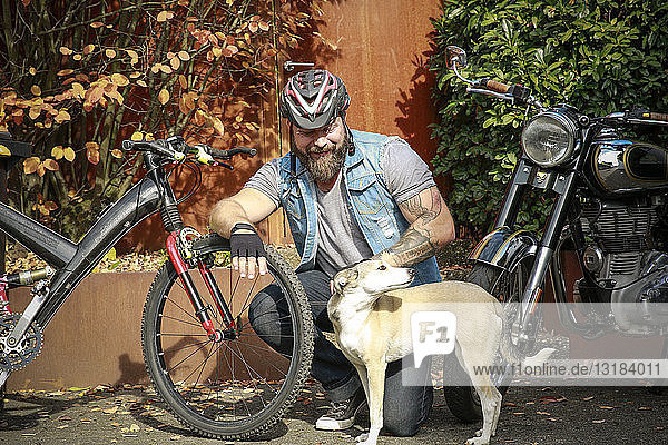 Lächelnder Mann mit Hund zwischen Motorrad und Fahrrad