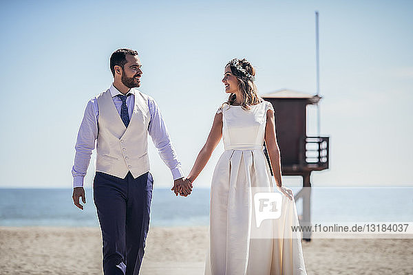 Happy bridal couple walking hand in hand on the beach