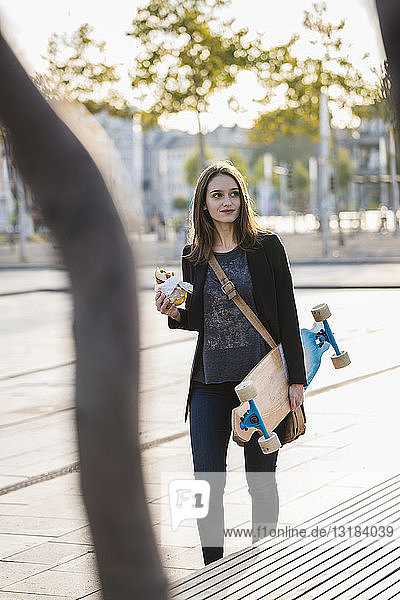 Junge Frau mit Longboard in der Stadt in Bewegung