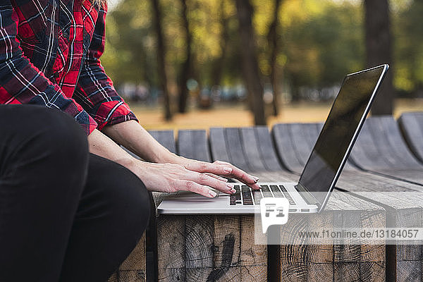 Junge Frau sitzt auf Bank im Freien und arbeitet am Laptop  Teilansicht