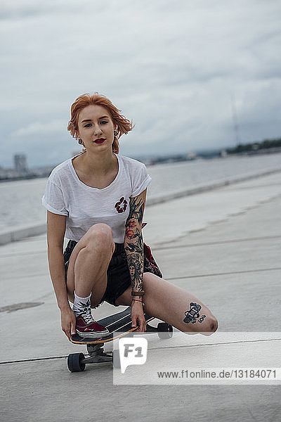 Porträt einer jungen Frau  die auf einem Carver-Skateboard auf einer Promenade kauert