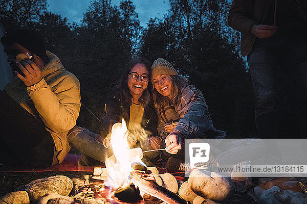 Gruppe von Freunden sitzt am Lagerfeuer und röstet Marshmallows
