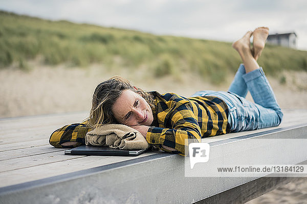 Mature woman with laptop  lying on boardwalk at the beach  relaxing