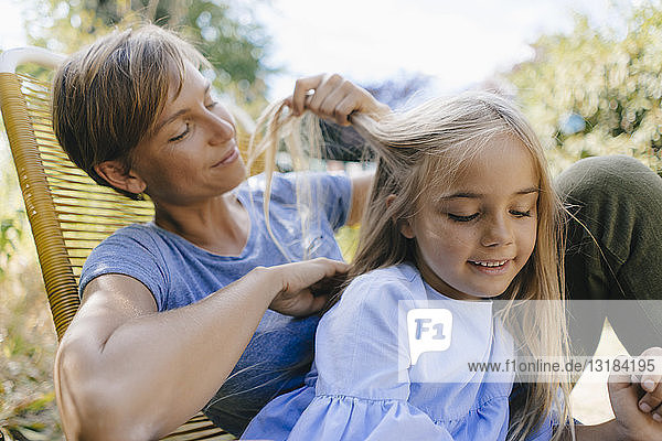 Mutter flechtet im Garten die Haare ihrer Tochter
