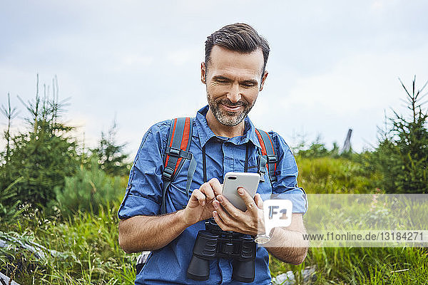Lächelnder Mann überprüft sein Handy während einer Wanderung