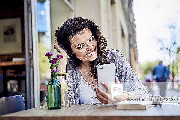 Happy woman looking at cell phone at outdoors cafe