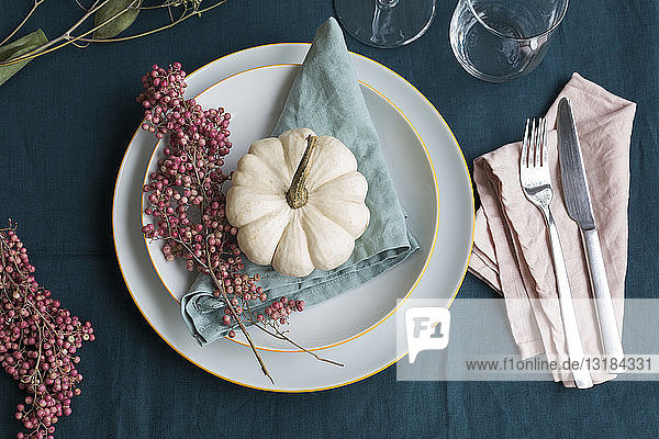 Herbstliche Tischdekoration mit weißem Zierkürbis und rosa Pfefferkörnern