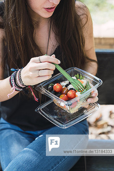 Young woman sitting in a park  eating salad