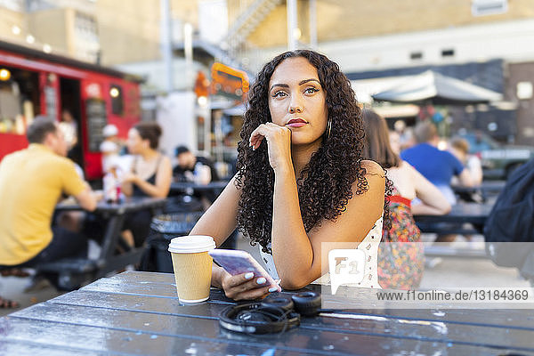 Hübsche junge Frau mit Handy am Tisch sitzend und wartend