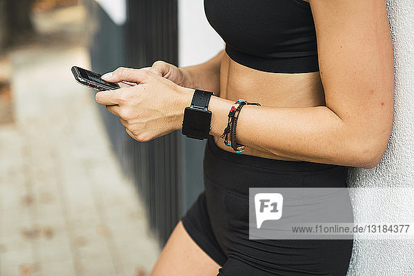 Passende junge Frau mit einer Smartwatch  die ein Smartphone benutzt