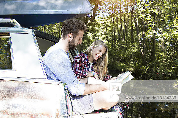 Lächelndes junges Paar mit Karte und Kanu im Auto an einem Bach