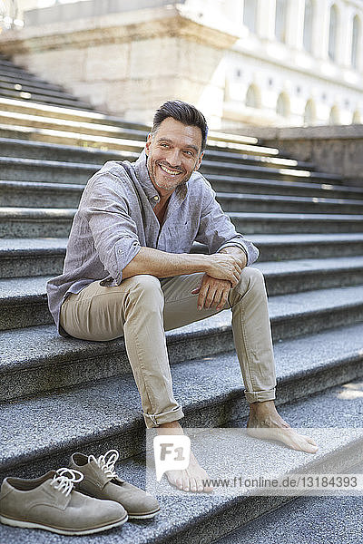 Porträt eines lächelnden reifen Mannes  der barfuss auf einer Treppe sitzt