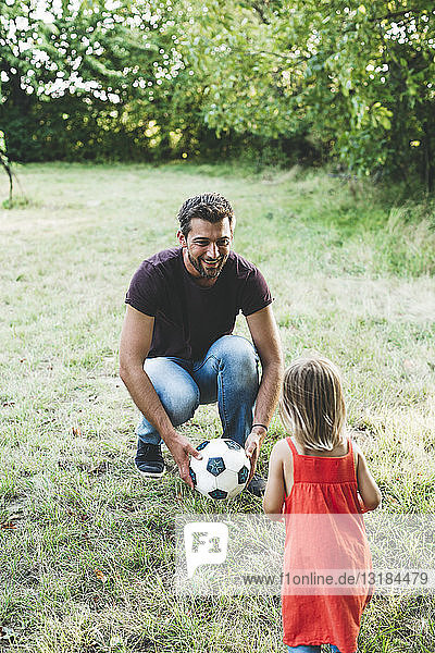 Glücklicher Vater spielt mit Tochter auf der Wiese Fussball