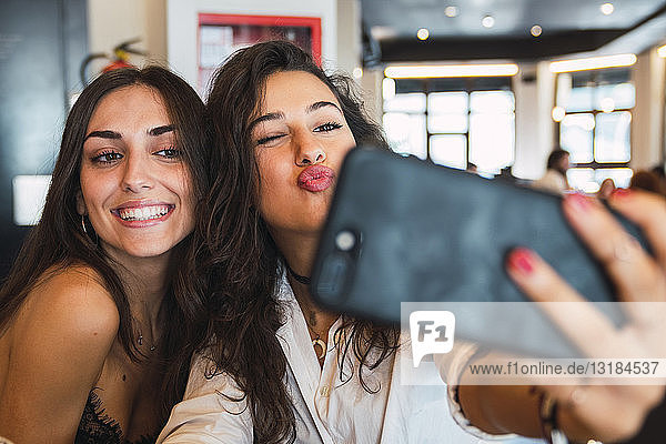 Portrait of two friends taking selfie with smartphone in a coffee shop having fun