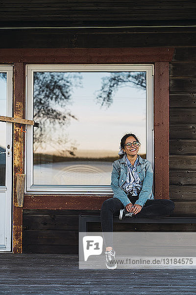 Glückliche junge Frau sitzt auf der Veranda eines Holzhauses
