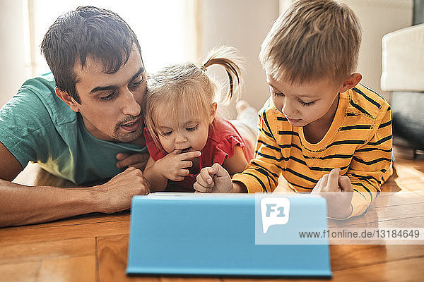 Vater und seine Kinder liegen zu Hause auf dem Boden und benutzen ein digitales Tablett
