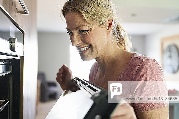 Lächelnde Frau beim Kochen in der Küche schaut in den Ofen