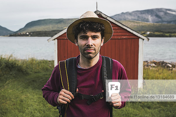 Young man with backpack exploring red barn in Northern Norway
